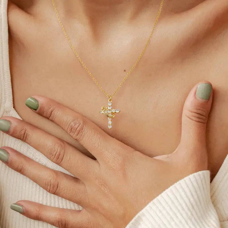 Gold necklace with a cross pendant worn by a person, with a hand touching the chest.