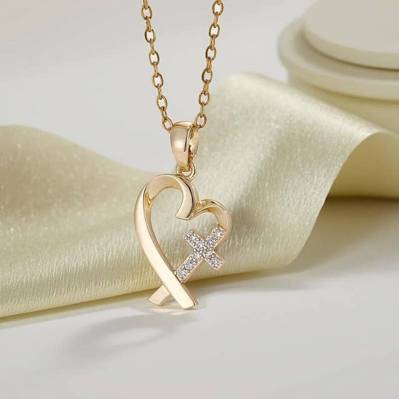Gold necklace with a heart and cross pendant on a soft fabric background