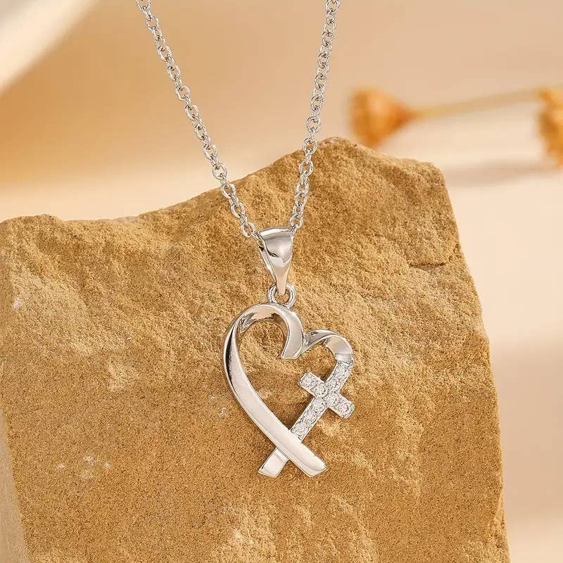 Silver heart and cross pendant necklace on a stone surface