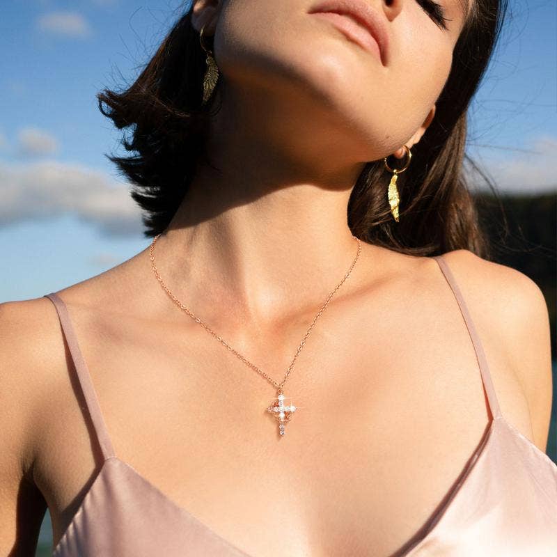 Woman wearing a necklace with a cross pendant against a blue sky.
